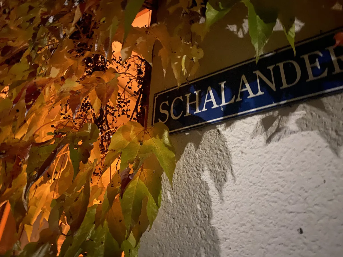 Das blaue Emailleschild „Schalander“ an der Hauswand, umrankt von herbstlich gefärbtem Wein